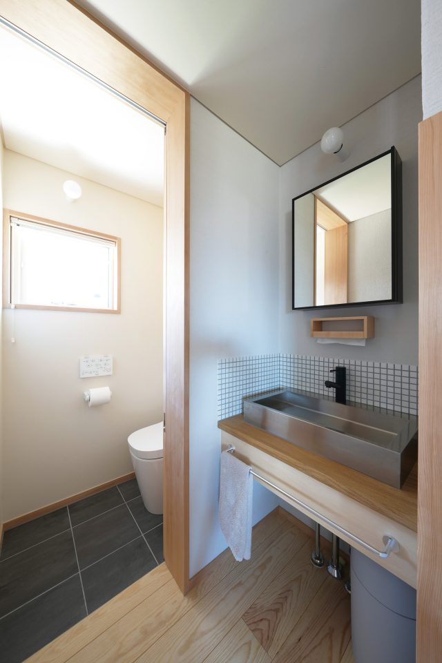 トイレの床のタイルは1階の洗面所やストーブ周りの床と統一。 シャープな印象のステンレスの洗面が空間を引き締めています。