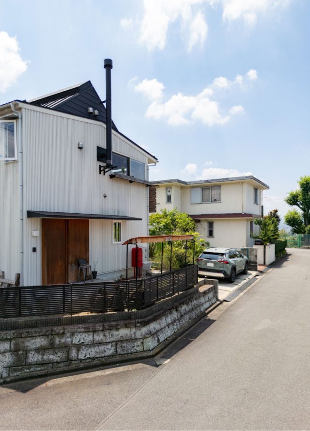 丘の上、上に遮るものがなく美しい青空が広がる。白い外壁に薪ストーブの煙突と赤いポストがポイントに。