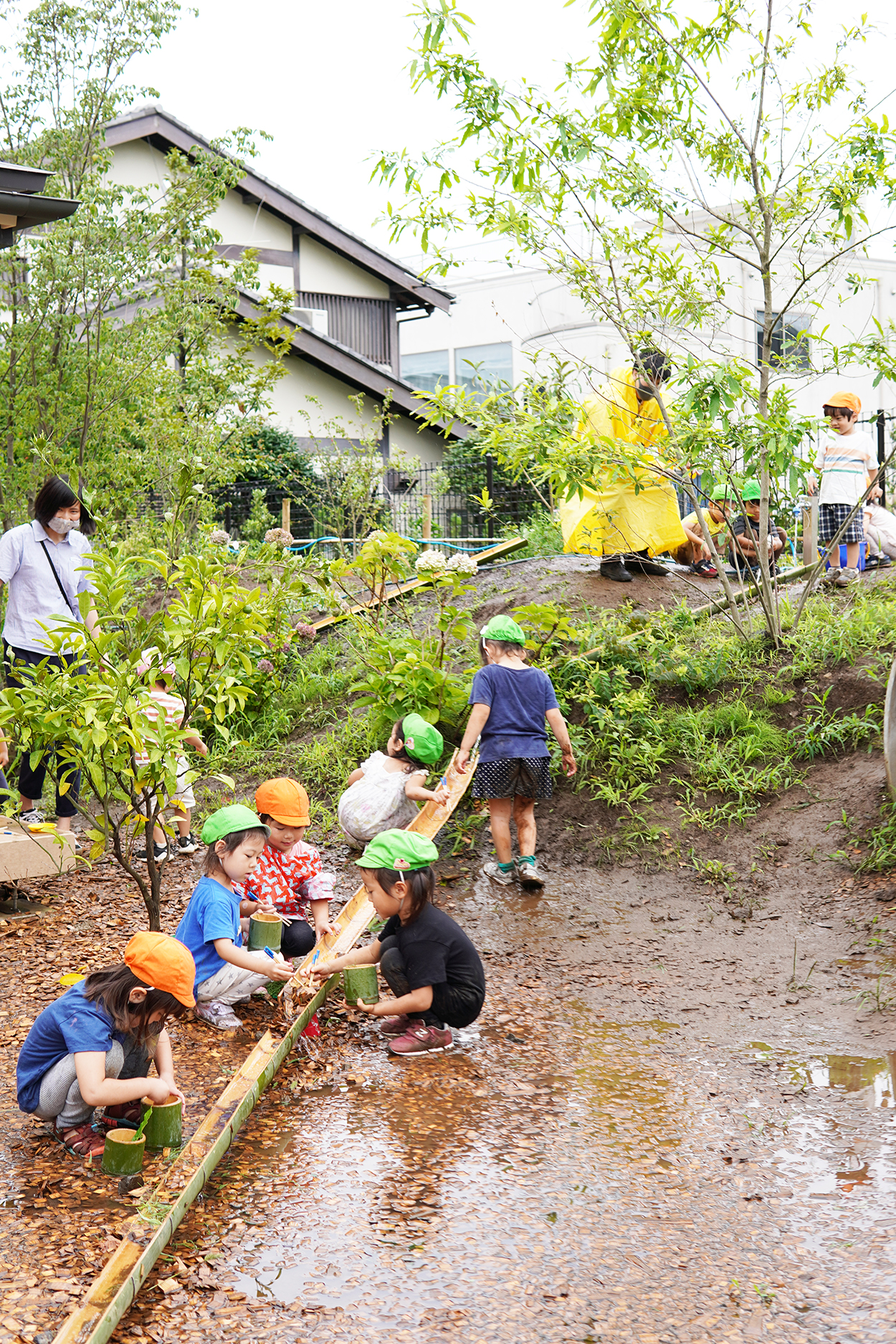 斜面を利用した流しそうめんごっこ。竹筒に葉っぱや木の実を流す人、それをすくう人と、役割分担が自然に行われています。