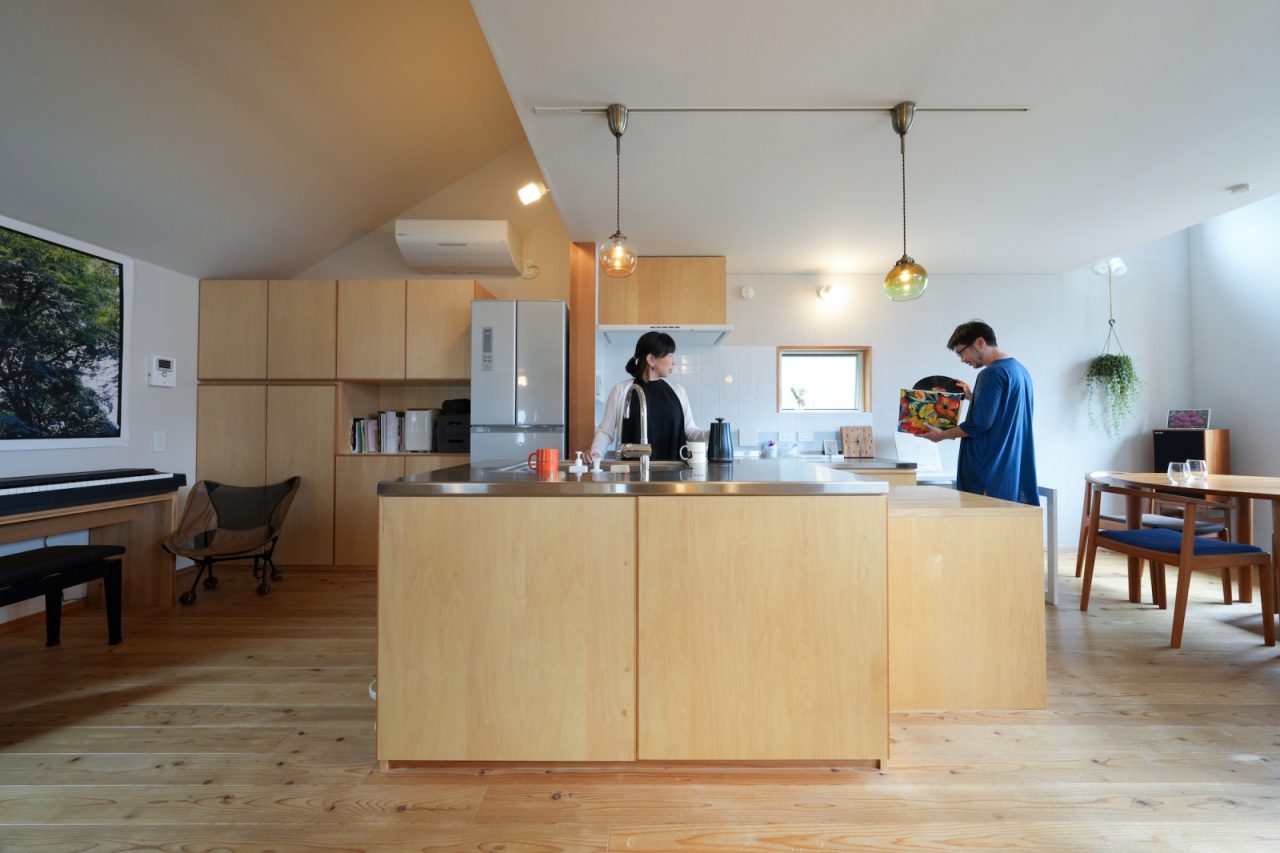 全てを見渡せるコントロールタワーのようなアイランドキッチン。背面キッチンに吊戸棚は作らず、アイランドキッチンと奥の造作棚で収納量を確保しました。