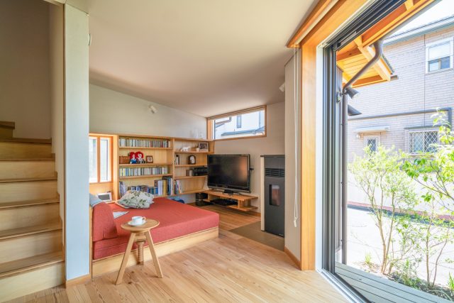 角のソファースペースにはペレットストーブも。ほぼ正方形ソファーからまさに“手を伸ばすと届く範囲”に本やDVDが並べられる棚が。