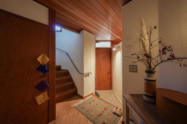 子世帯の玄関を新設。2つの玄関の間仕切り壁は上に隙間をつくり、互いの気配を少し感じられるようにしました。思わず触れたくなるようななめらかなアイアン手すり（既存）が自然と2階へいざないます。