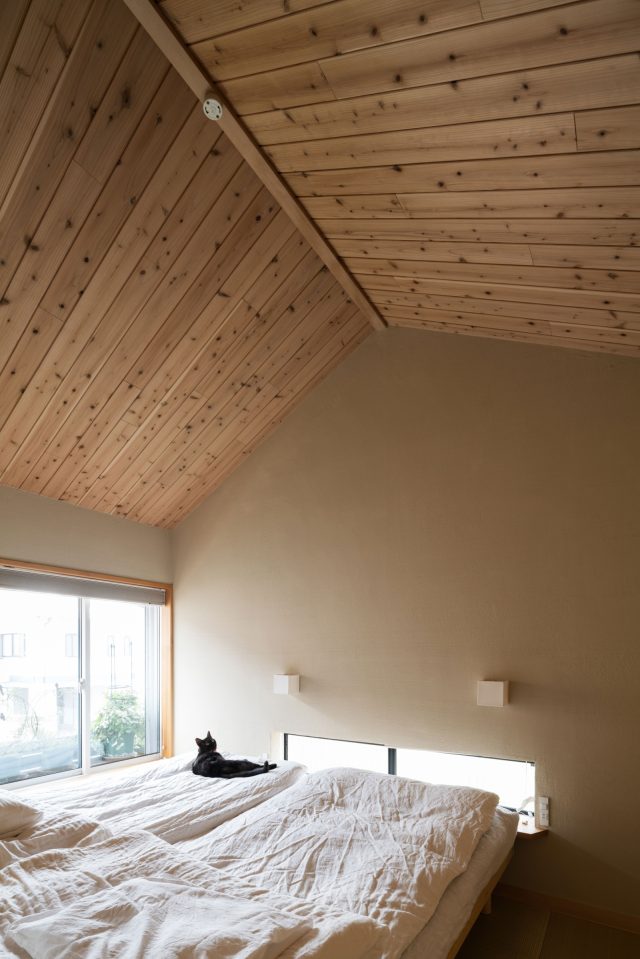 切妻屋根の勾配天井(カラマツ板張り)の寝室。