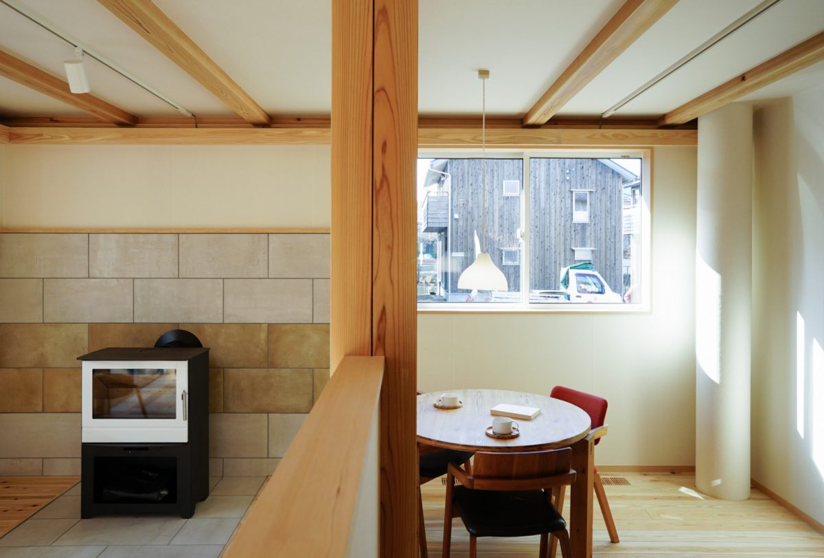 白い薪ストーブと壁面のタイルが印象的です。写真右のOMソーラーのダクトを通して屋根で集めた太陽熱を床下に送っていきます。