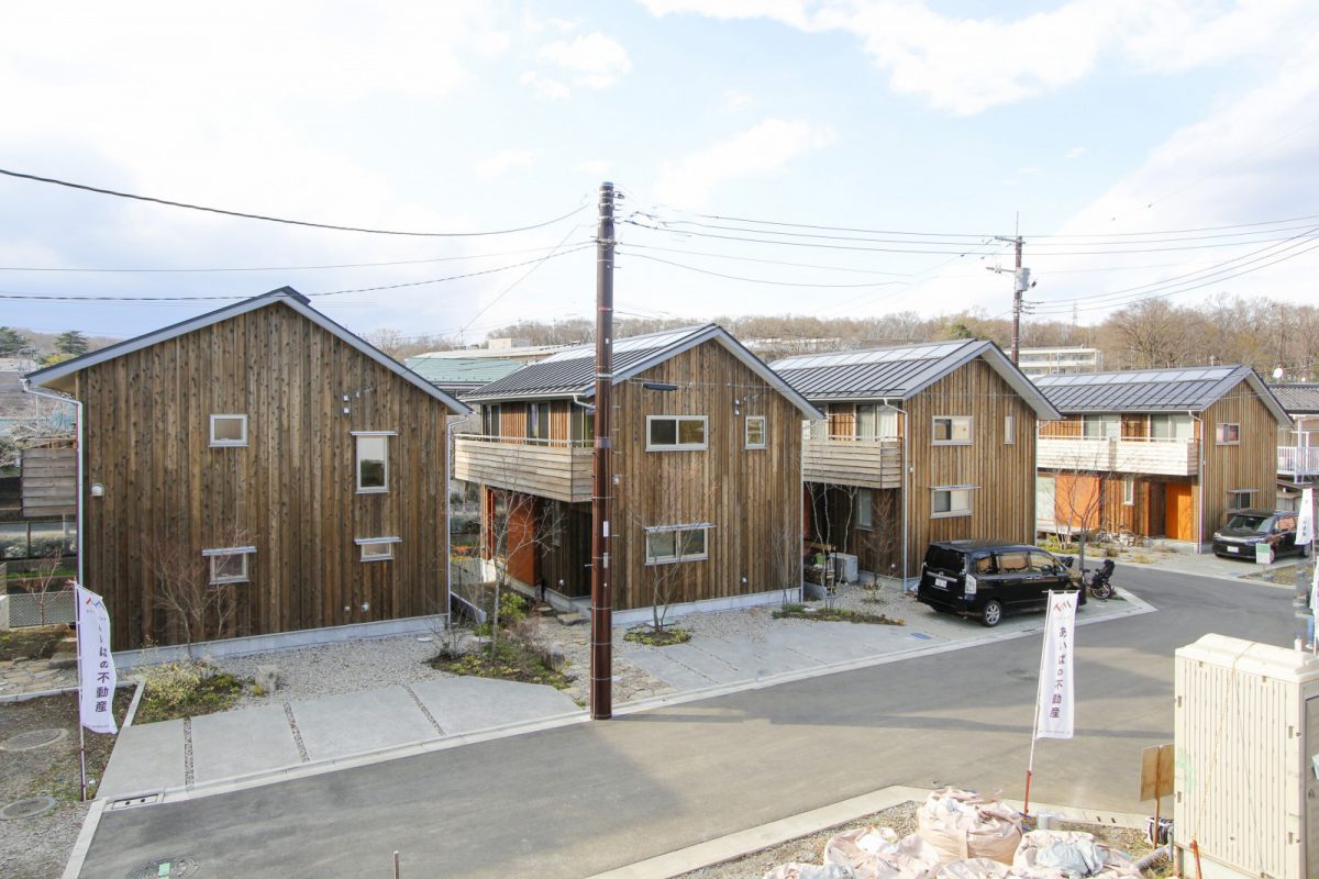 二階から八国山緑地が眺められます。タウンの建物は外壁の杉板張り仕上げと木製ドアで統一。全棟にOMソーラーを搭載し、小林賢二さんが造園デザインを行っています。Kさんの家は、9区画のソーラータウン八国山に5棟目として完成するお住まい。