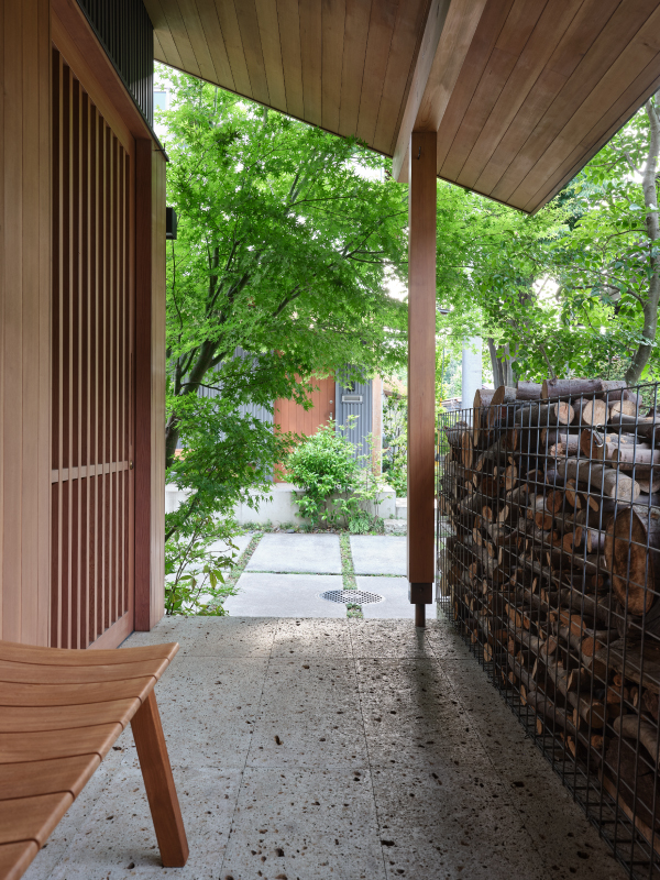 玄関前の薪棚は、北風を防ぐと同時に、道路からの目線を緩やかに遮ります。深い庇とベンチは、落ち着いて近所話ができ、置き配にも便利です。